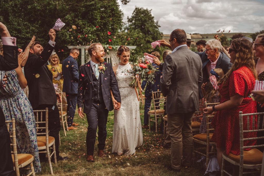 A wedding couple being showered with confetti as they walk the aisle at the end of their humanist ceremony