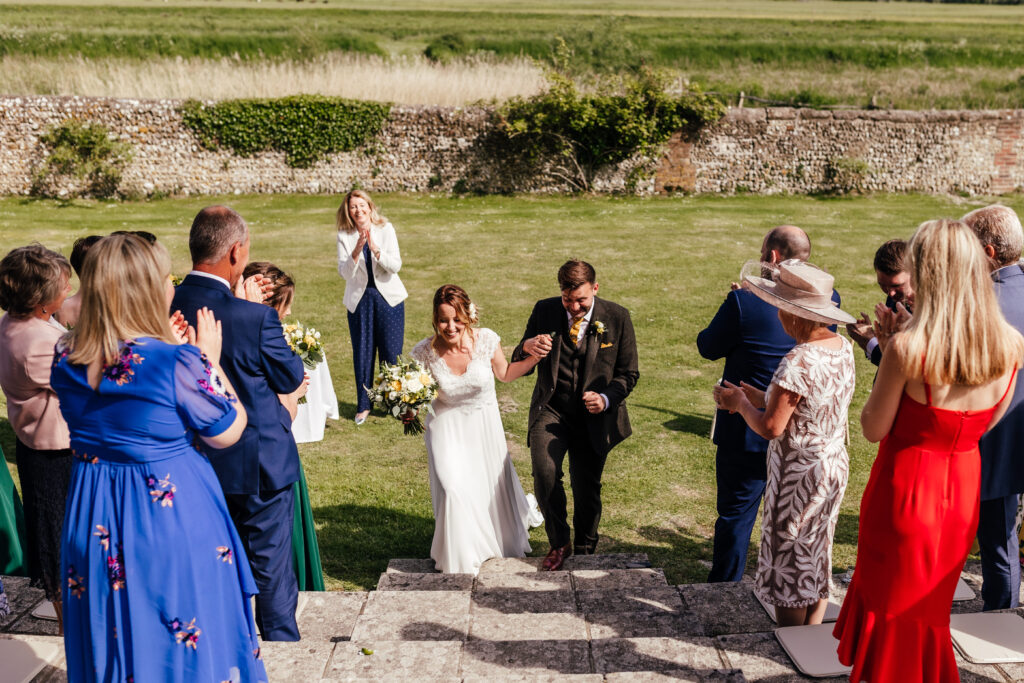 A newly married couple about to walk the aisle at the end of their humanist wedding ceremony, to the delight and applause of their guests.